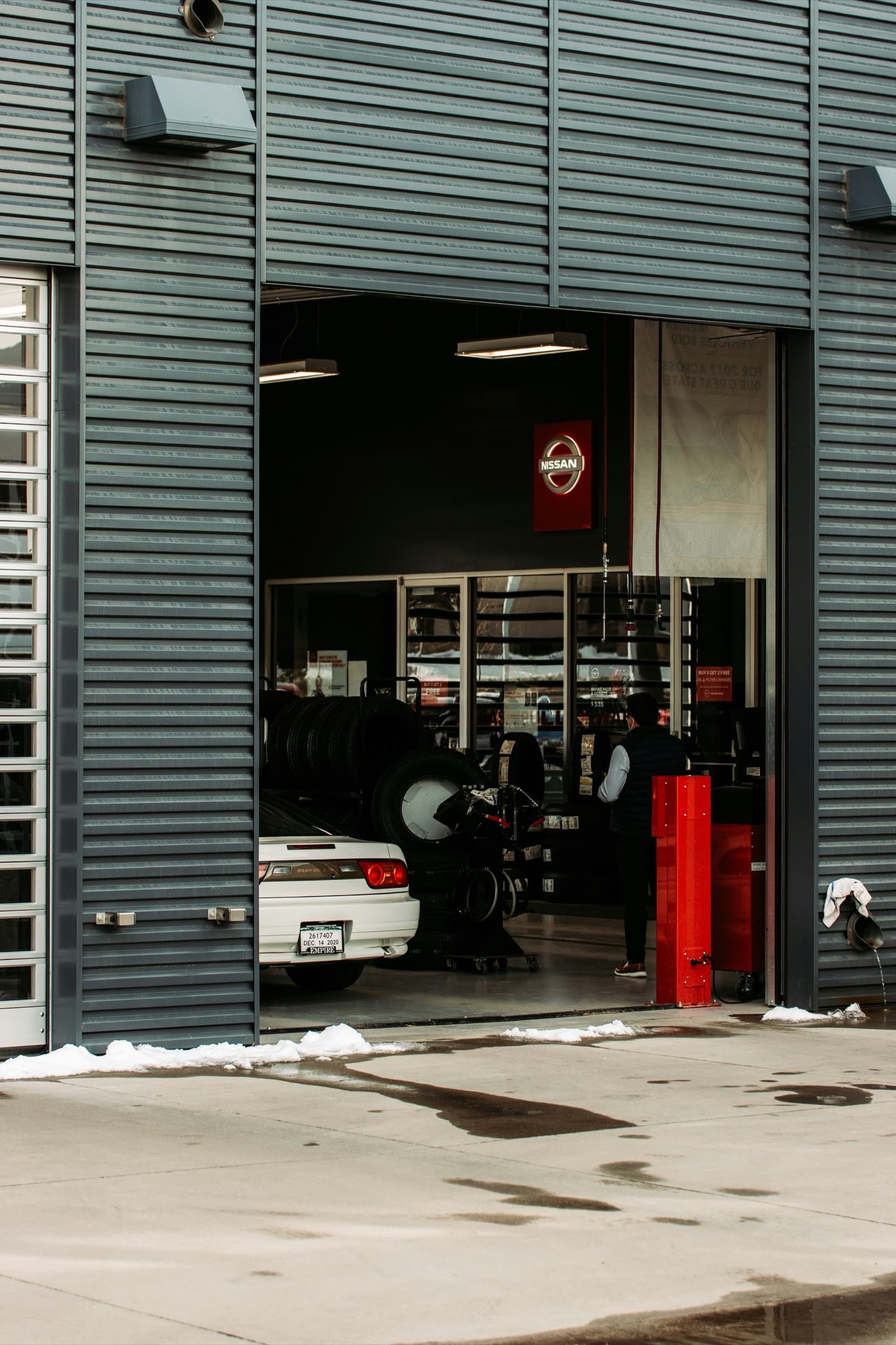 Open roller door of an auto service workshop with cars, tyres and equipment inside