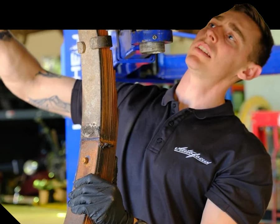 An Autofocus technician in Nelson reaching up under a vehicle on a hoist, holding a leaf spring