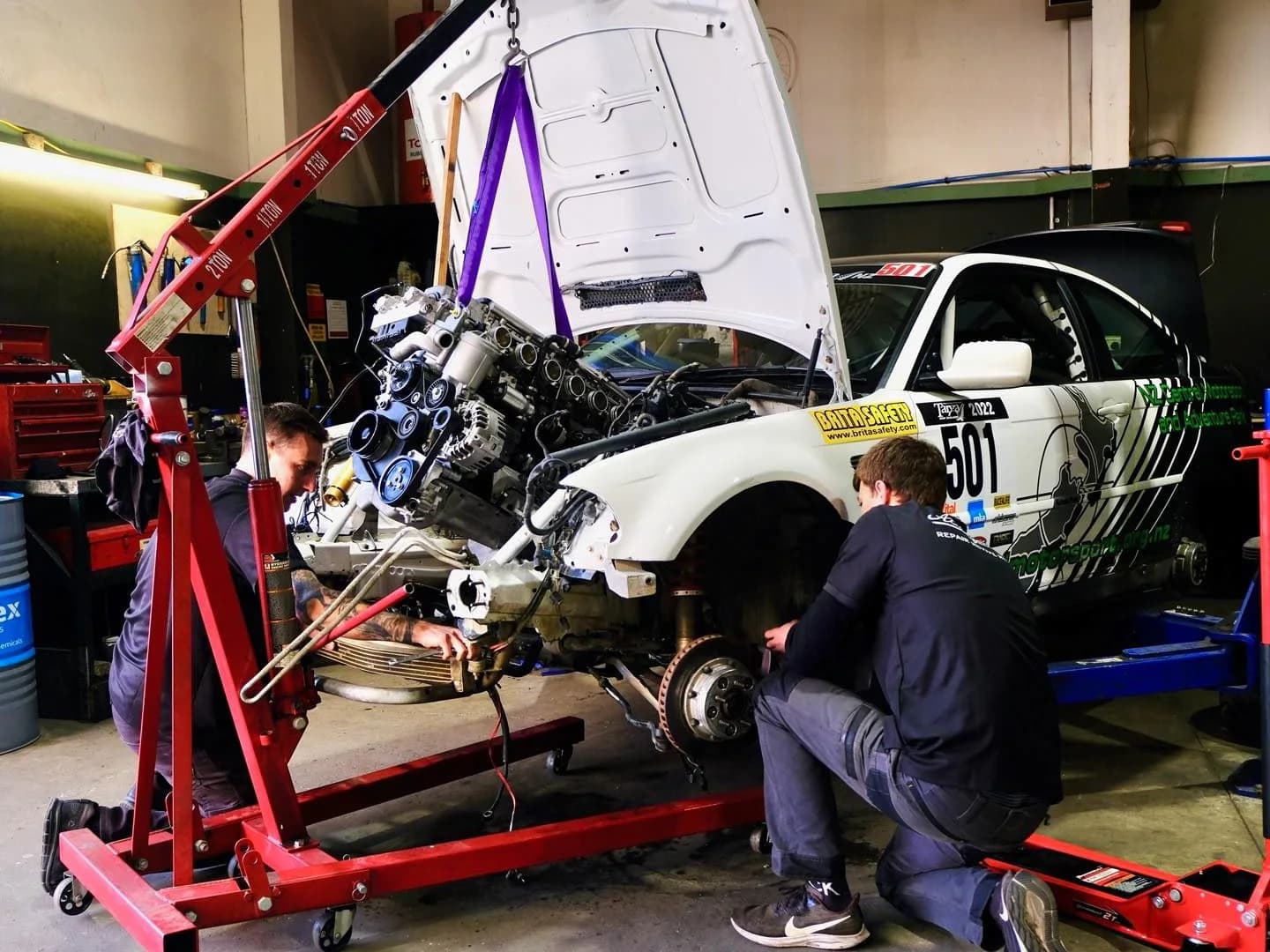 Two technicians at Autofocus in Nelson lifting the engine out of a rally car with an engine crane