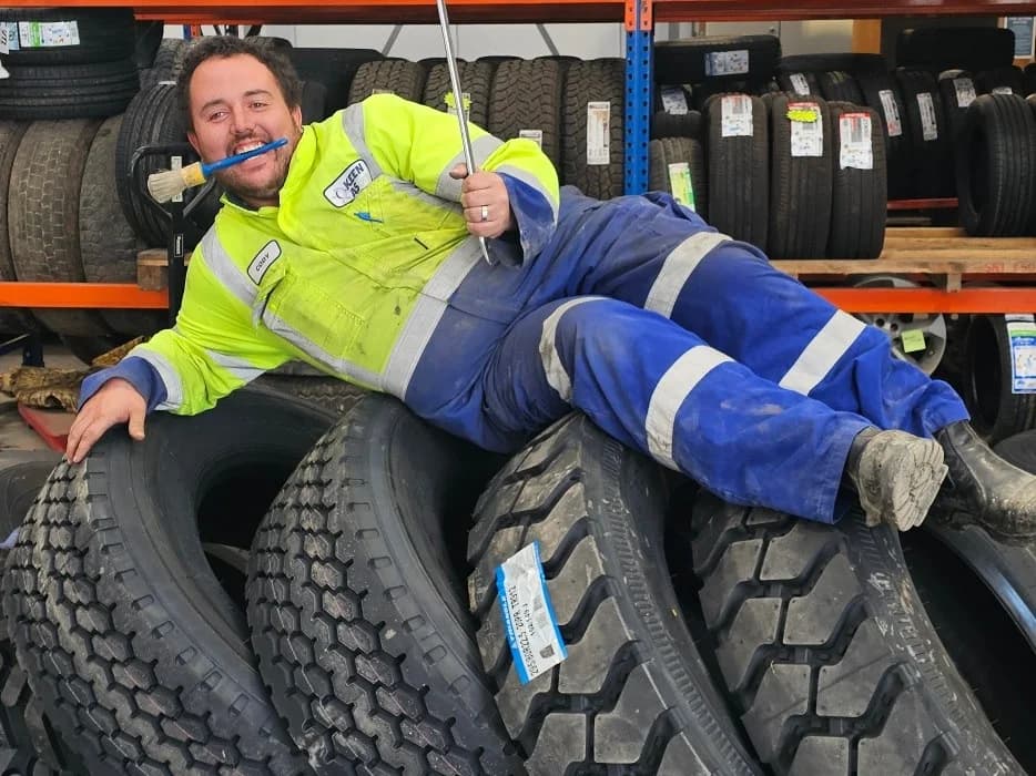 A Keen As Tyres technician in hi-vis lying across a stack of truck tyres in their tyre store