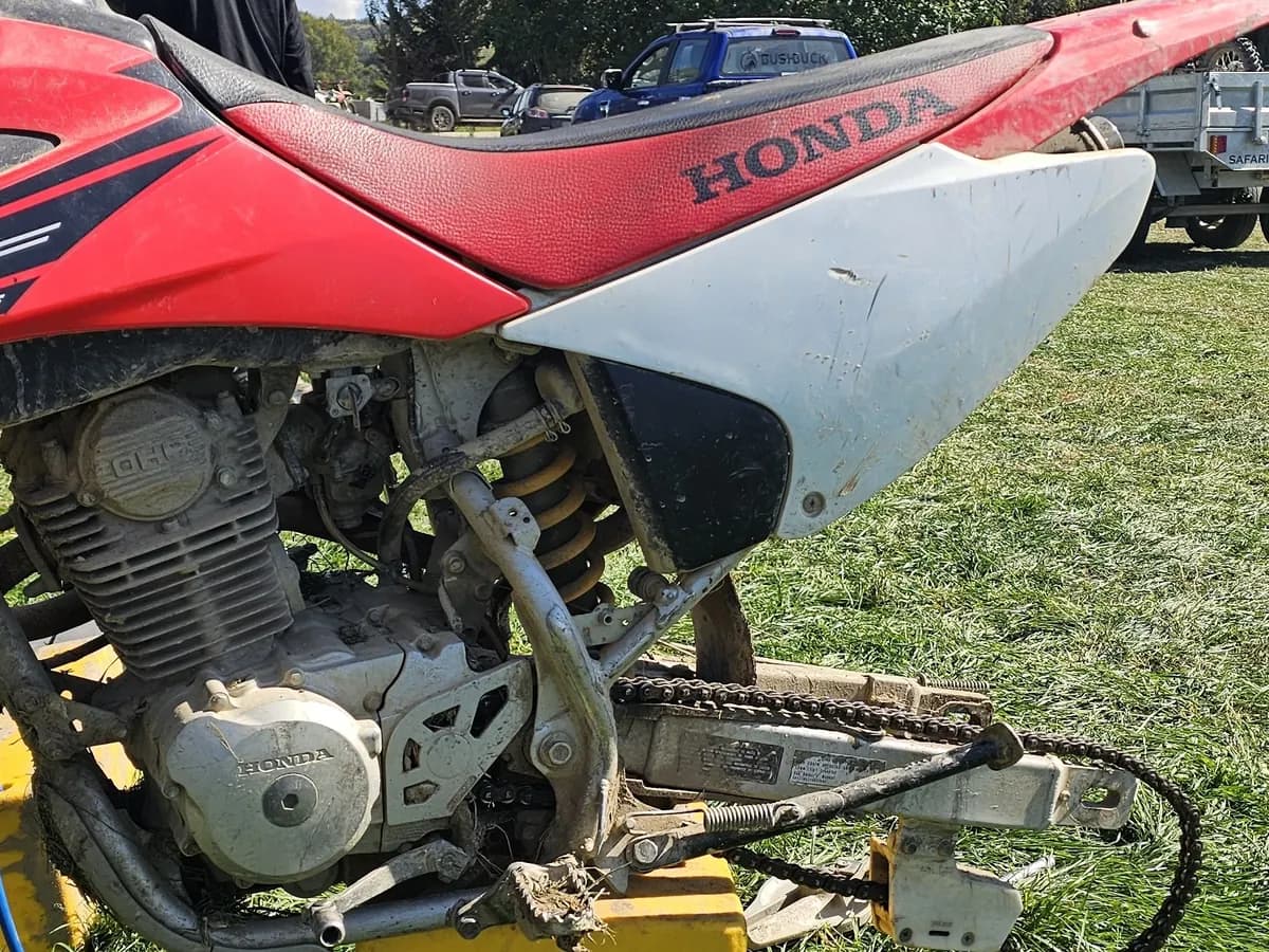 A red and white Honda dirt bike on a yellow stand in a paddock, its rear wheel off